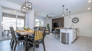 Una cocina moderna con una isla central, un comedor con mesa y sillas de madera, y un amplio ventanal que proporciona luz natural.