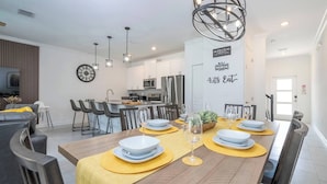 Cocina moderna con armarios blancos, una isla central y un comedor con manteles individuales amarillos y platos blancos.