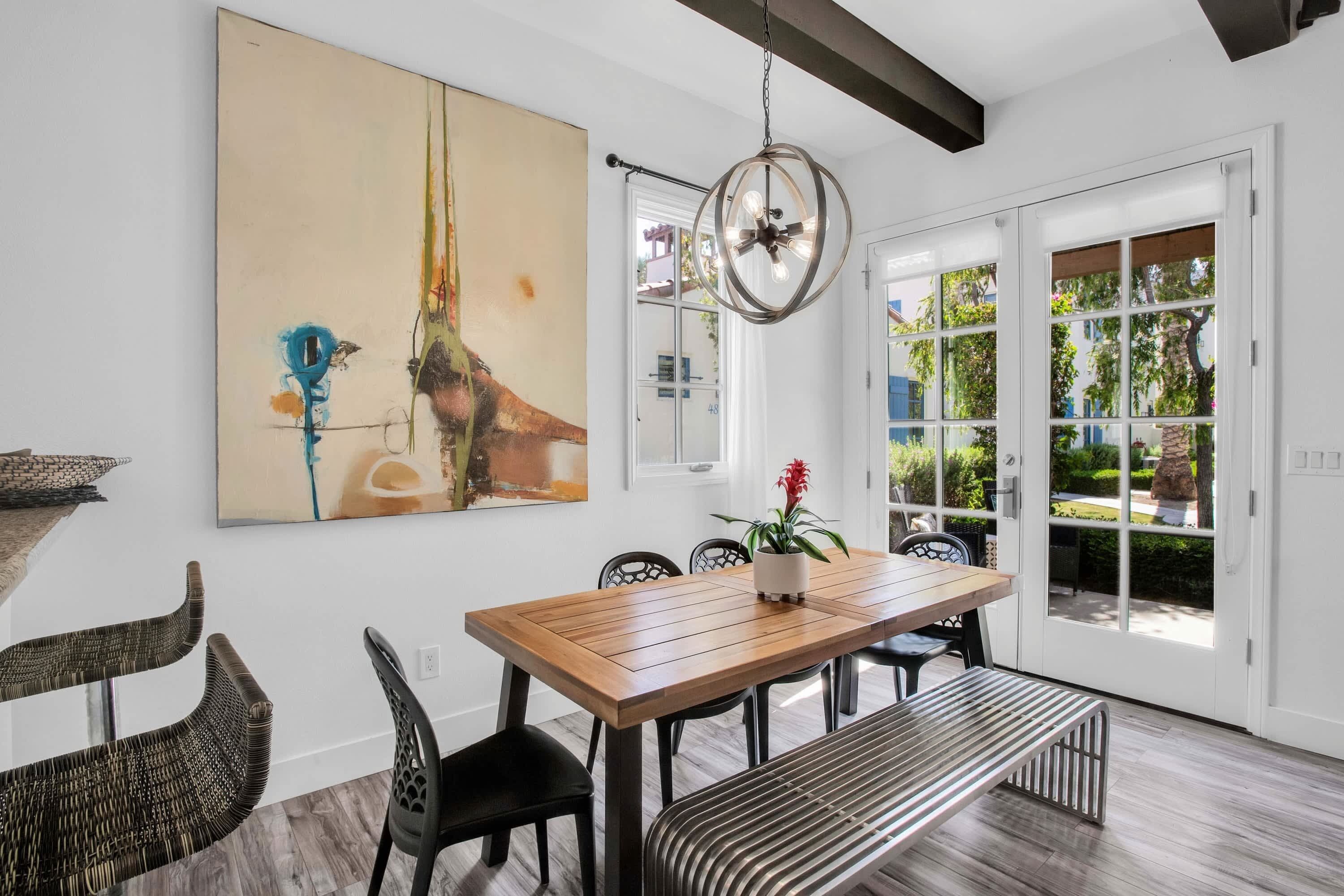 A dining area with a wooden table, black chairs, a bench, and a large abstract painting on the wall.