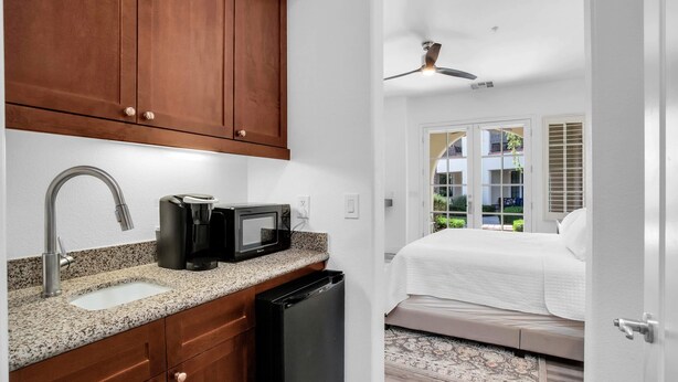 A compact bedroom with a bed, a window with blinds, and a view of a balcony.