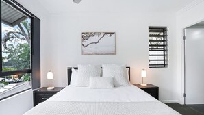A bedroom with a large bed, two bedside tables with lamps, a window with blinds, and a painting on the wall.