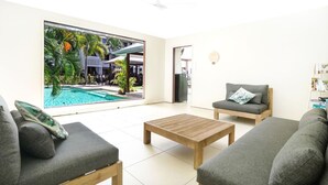 A modern living room with a large glass door leading to a pool area, grey sofas, and a wooden coffee table.