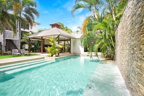 Una piscina con agua cristalina, rodeada de palmeras y un porche cubierto.