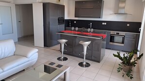 A modern kitchen with a central island, stainless steel appliances, and a red countertop. - Location vue mer Saint Raphaël (Saint-Raphaël)
