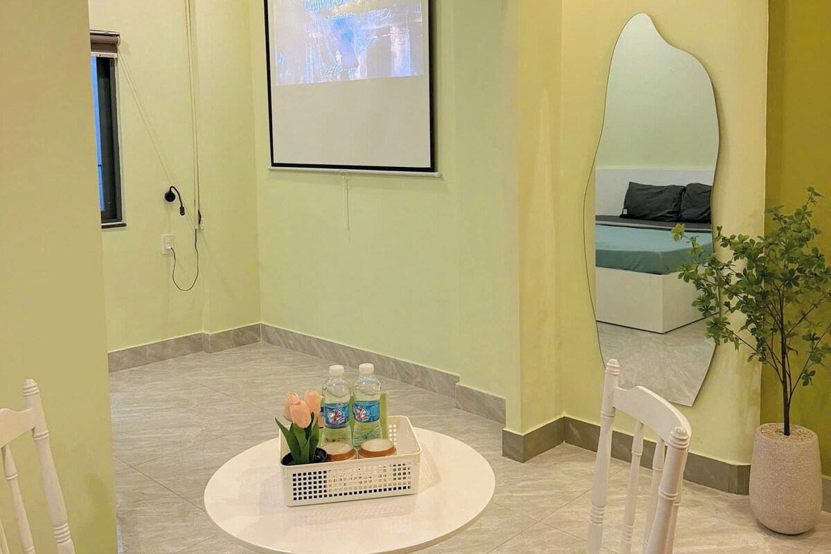 A conference room with a projection screen, a round table with chairs, and a potted plant.