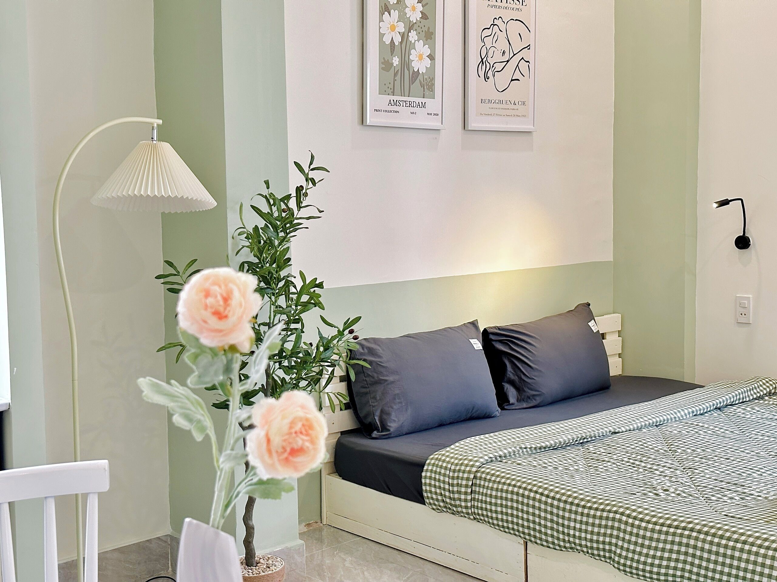 Een slaapkamer met een bed, kussens, een lamp en een plant in een pot.