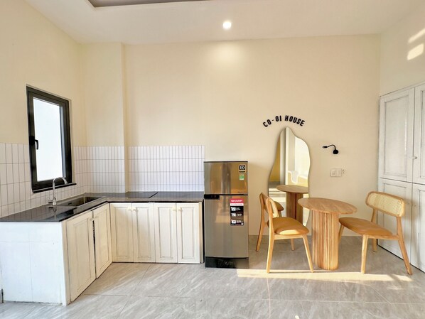 A modern kitchen with a built-in island, a stainless steel refrigerator, and a dining area with a wooden table and chairs. - Corgi House Danang (Da Nang)