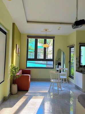A spacious room with a large window, a red sofa, a white chair, and a small table. - Corgi House Danang (Da Nang)