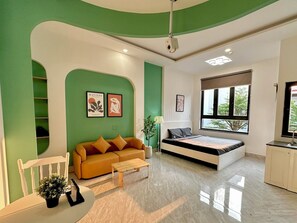 Ein modernes Wohnzimmer mit Sofa, Couchtisch und Bett. An den Wänden sind Kunstwerke und ein Fenster mit Blick.