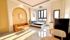 A modern living room with a sofa, a dining table, a TV, and a window with a city view. - Corgi House Danang (Da Nang)