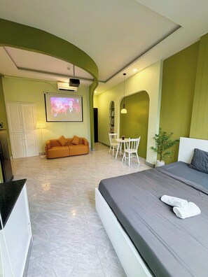 A hotel room with a bed, a sofa, a dining table with chairs, a TV screen, and a small potted plant. - Corgi House Danang (Da Nang)