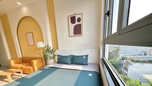 A hotel room with a bed, a sofa, a lamp, and a view of the city. - Corgi House Danang (Da Nang)
