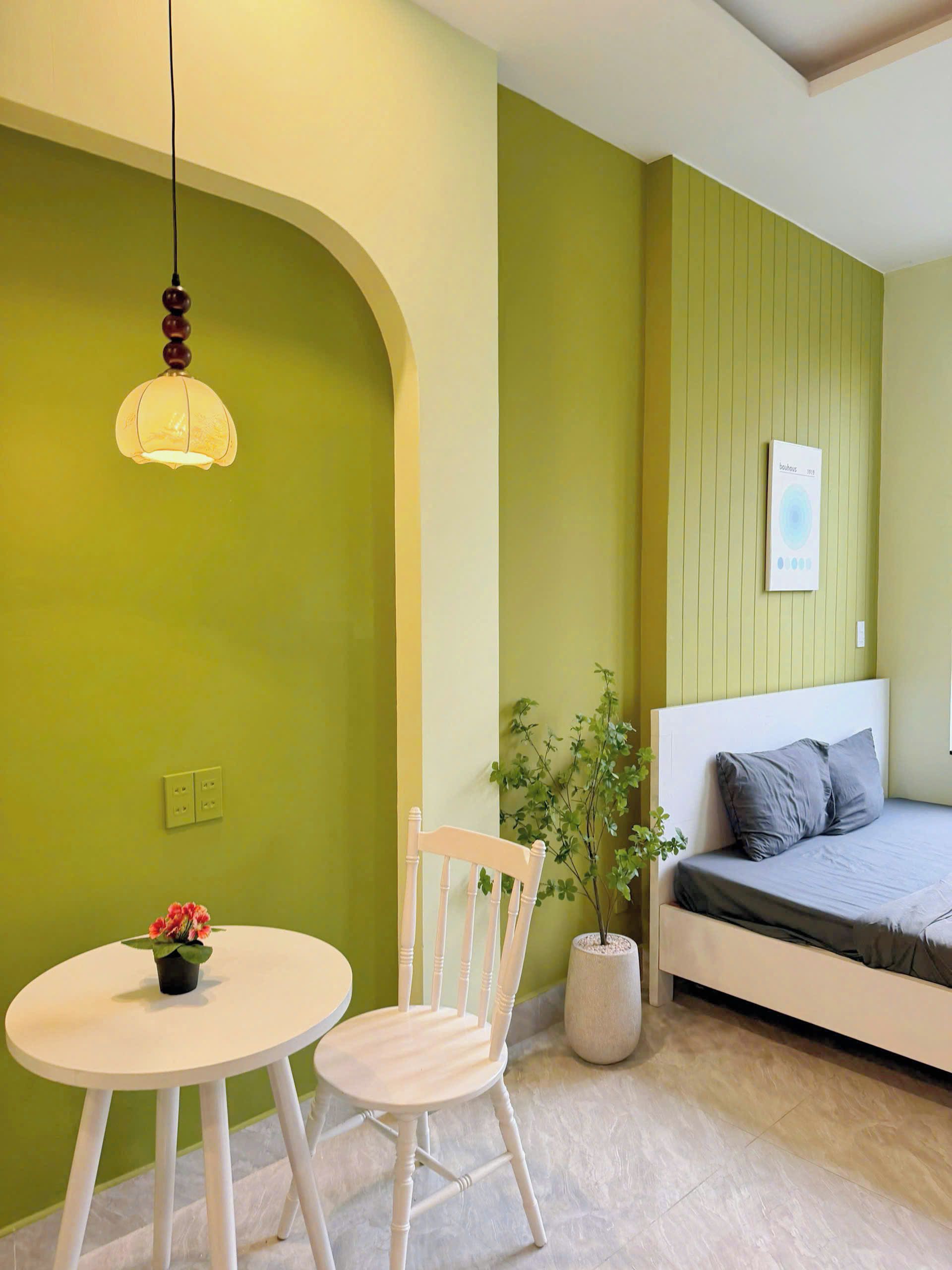Quarto com cama, mesa com cadeira, luminária pendente, quadro na parede e planta em vaso.