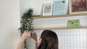 A person using a tablet in a kitchen with a red appliance, a plant, and a framed picture on the wall. - Corgi House Danang (Da Nang)