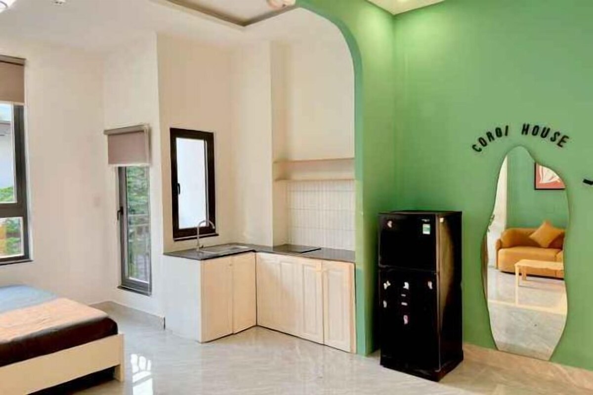 A compact room with a kitchenette, a bed, and a green accent wall.