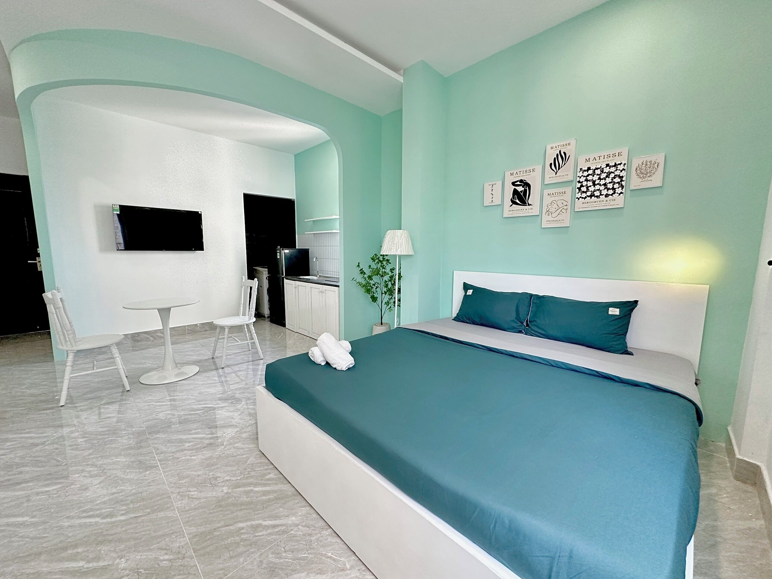 A modern hotel room with a large bed, a desk, and a chair. There are wall art pieces and a TV on the wall.