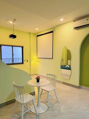 A room with a dining table, chairs, a projector, a large blank screen, a window with a view, and a mirror. - Corgi House Danang (Da Nang)