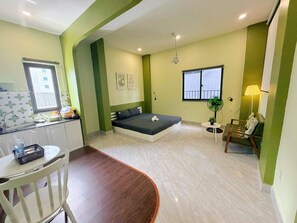 A compact room with a bed, a small table, a chair, a fan, and a window. - Corgi House Danang (Da Nang)
