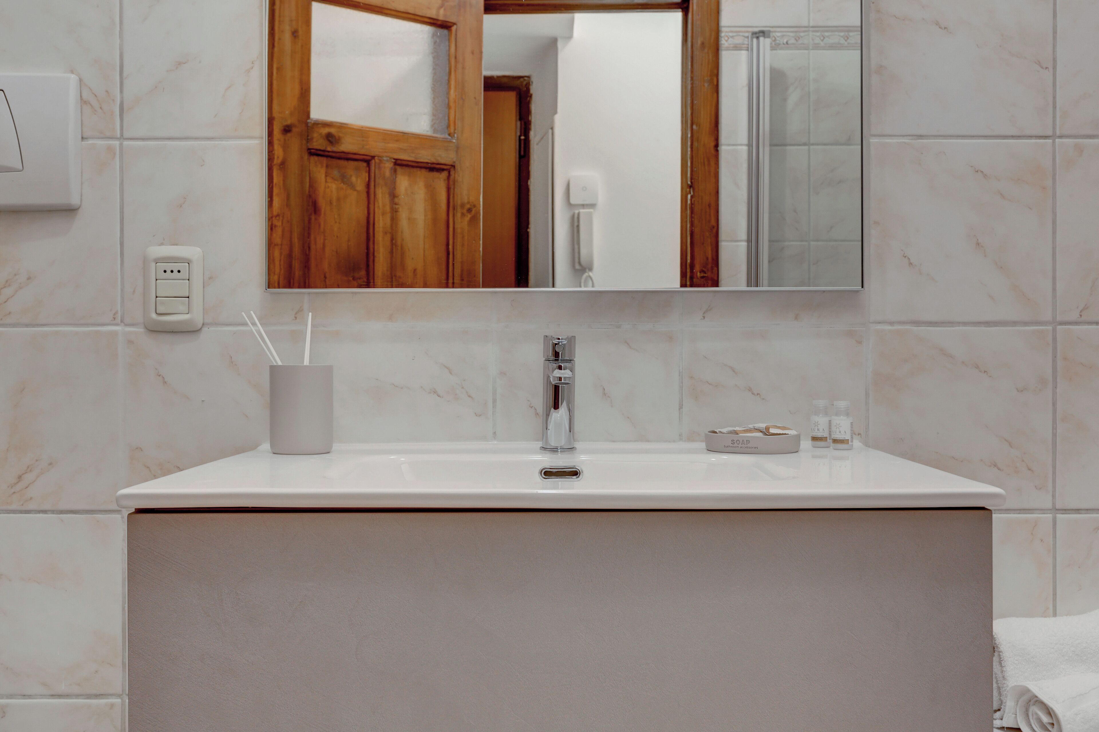 A bathroom with a white sink, a mirror, a wooden door, and a shower area.