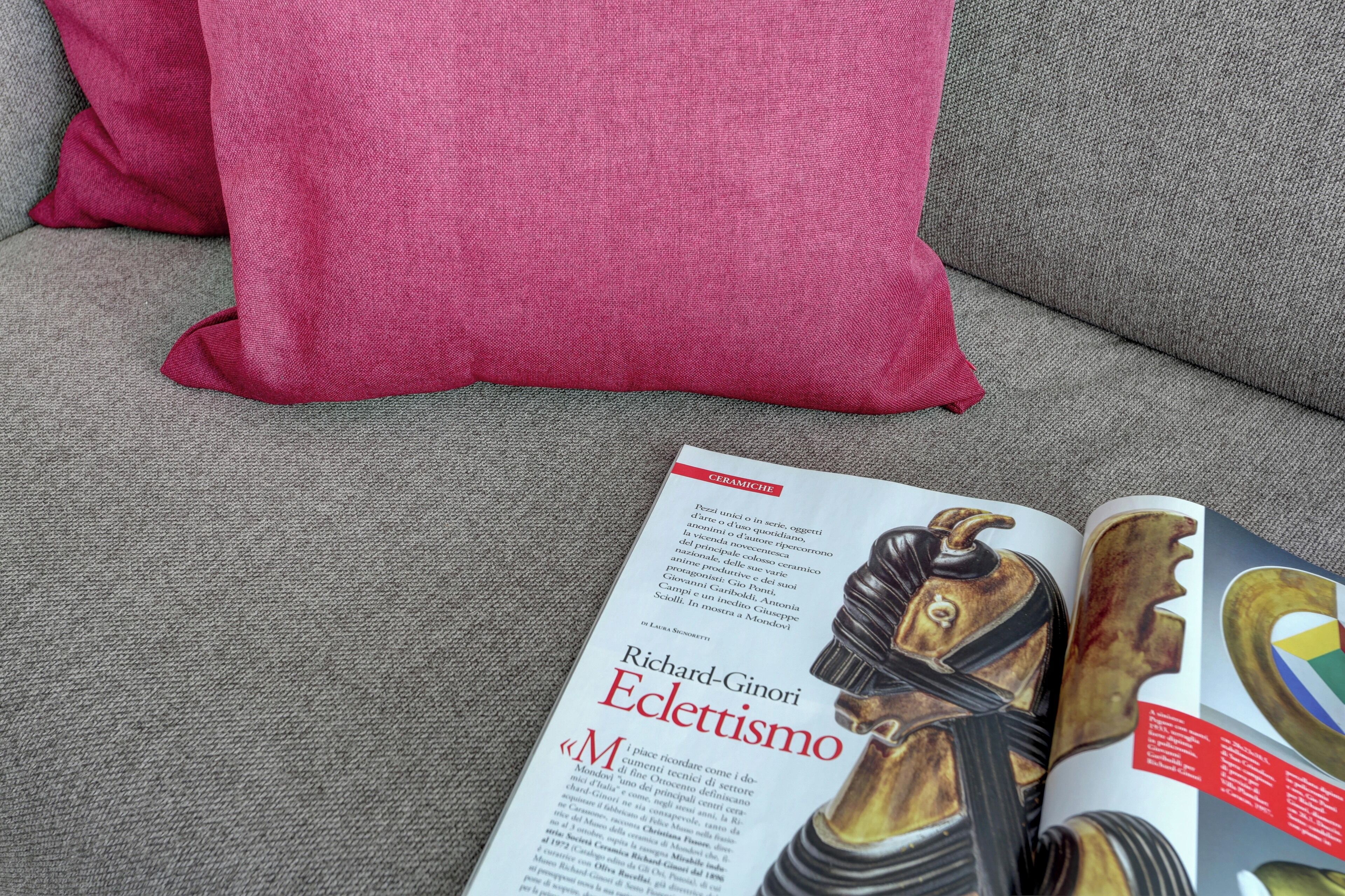 Un magazine posé sur un canapé gris, avec un coussin rose.