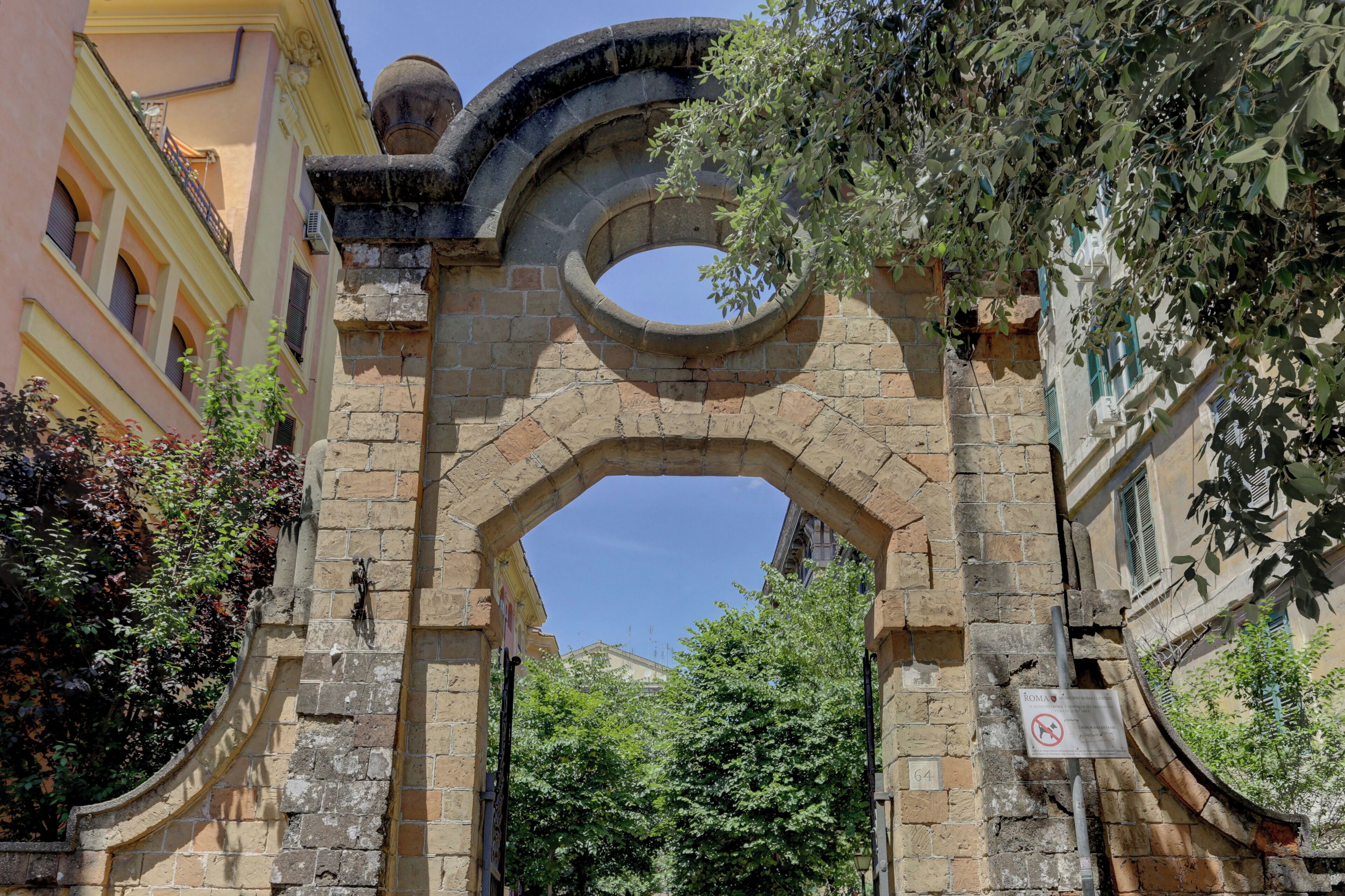 An arched stone gateway with a no parking sign, surrounded by buildings and trees.