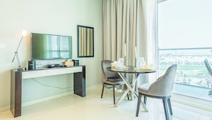 Een moderne hotelkamer met een groot raam, een eettafel met stoelen, een flatscreen televisie en een bureau met lamp.