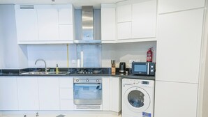 Een moderne keuken met witte kastjes, een roestvrijstalen fornuis, een inbouwoven, een wasmachine en een magnetron.