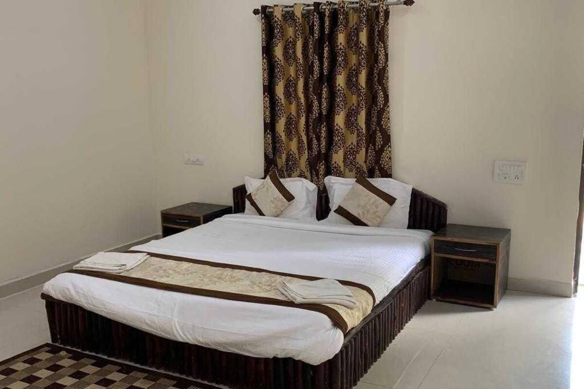 Un dormitorio con una cama grande, dos mesitas de noche, una cortina estampada y una alfombra de cuadros.