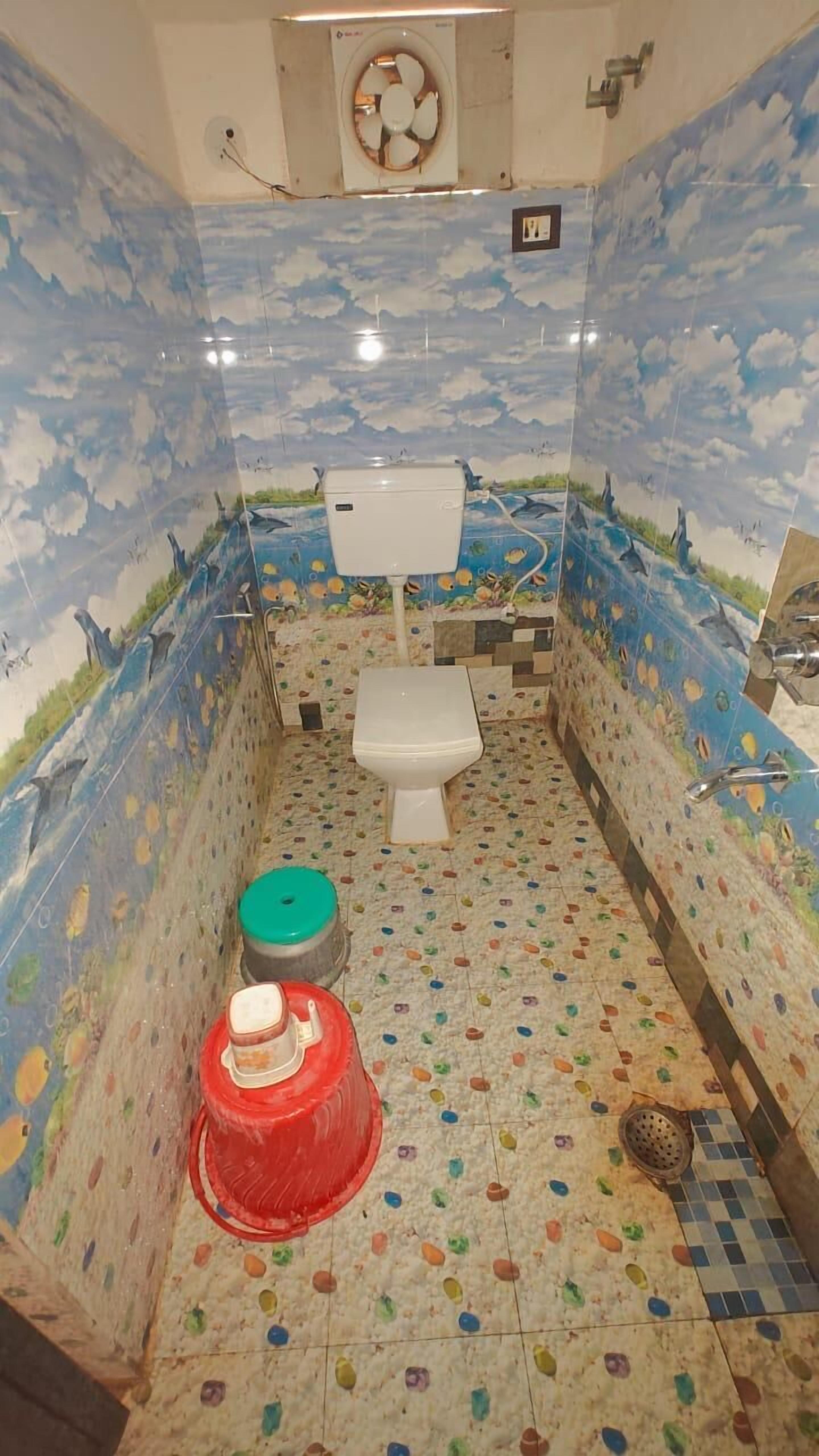 A bathroom with a toilet, a sink, and a shower area. The walls are decorated with a blue sky and clouds mural.
