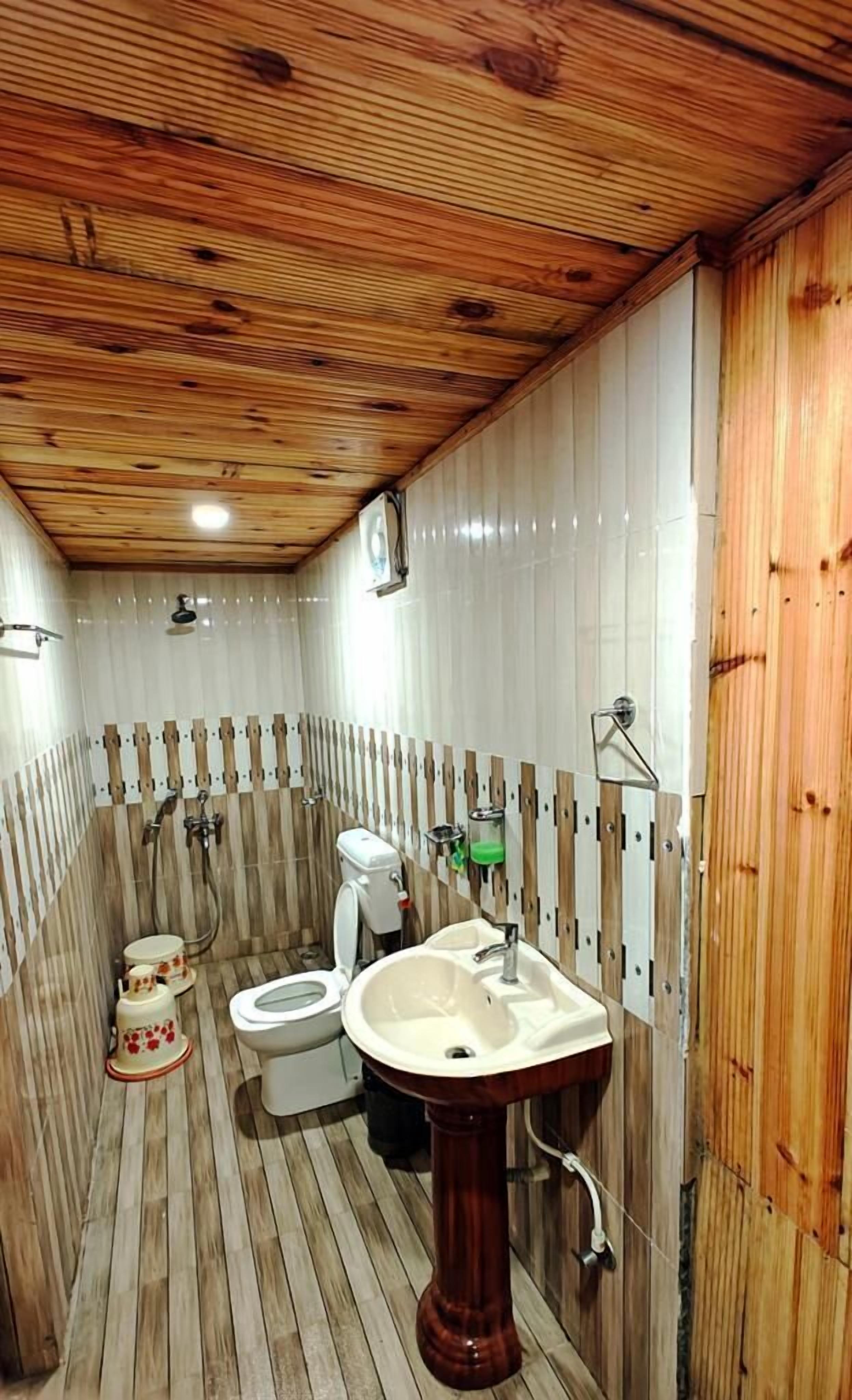 Une petite salle de bain avec un plafond en bois, des toilettes, un lavabo et un espace douche.