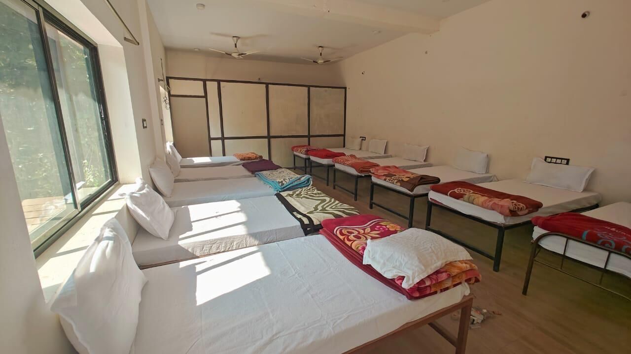 A room with multiple beds arranged in a row, large windows, and ceiling fans.