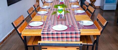 A dining area with a checkered tablecloth, wooden chairs, and a central table set with plates, glasses, and a pitcher.