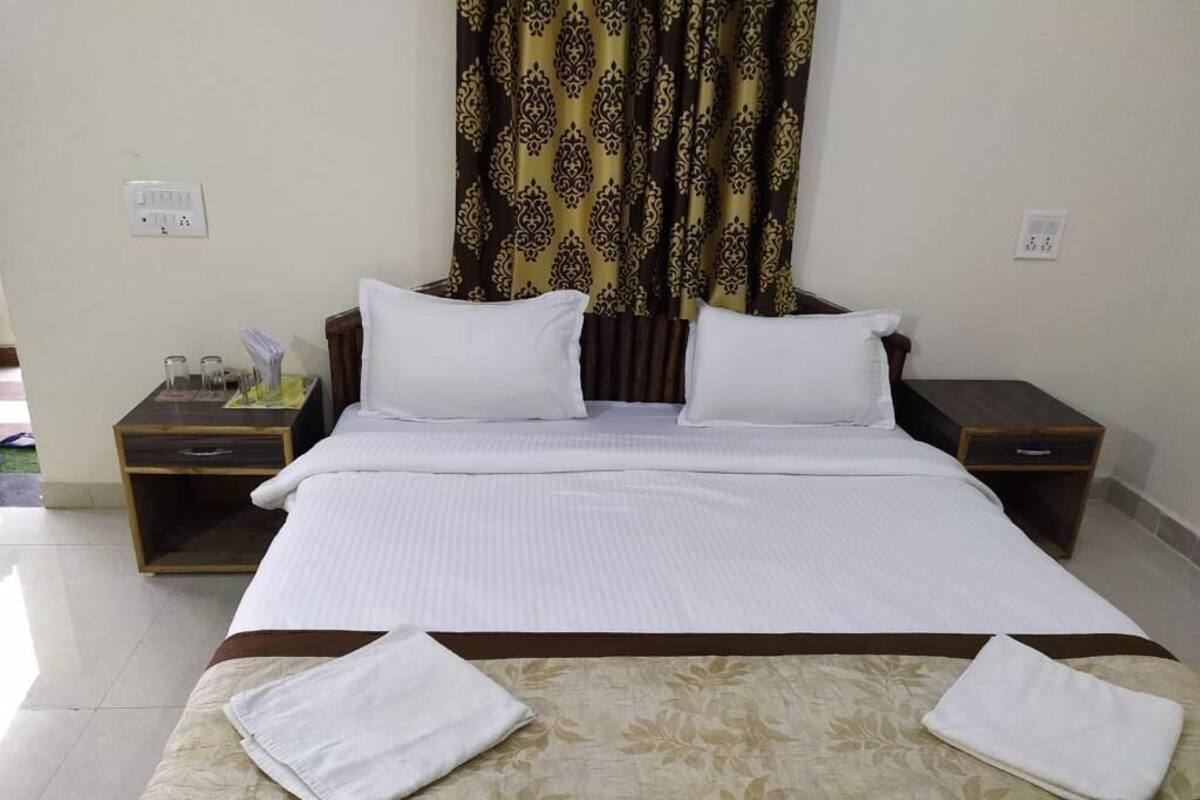 Una habitación de hotel con una cama grande, dos mesitas de noche y un ventanal con cortinas estampadas.