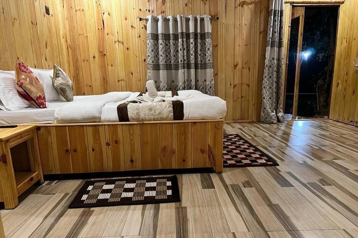 Una habitación con paneles de madera, una cama, una mesita y una alfombra estampada.