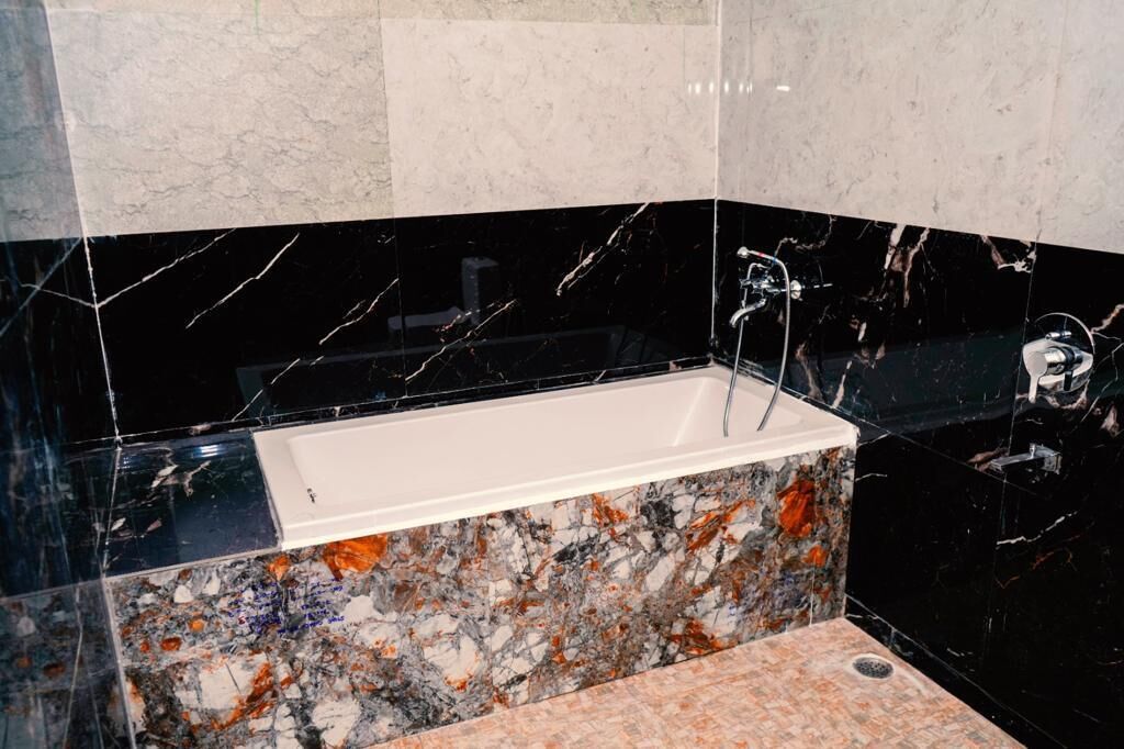 A modern bathroom with a black marble bathtub, a white sink, and a granite countertop.