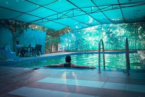 A pool area with a person lying on the edge, a covered seating area, and a view of trees. - Village Camp Pench National Park (Kurai)