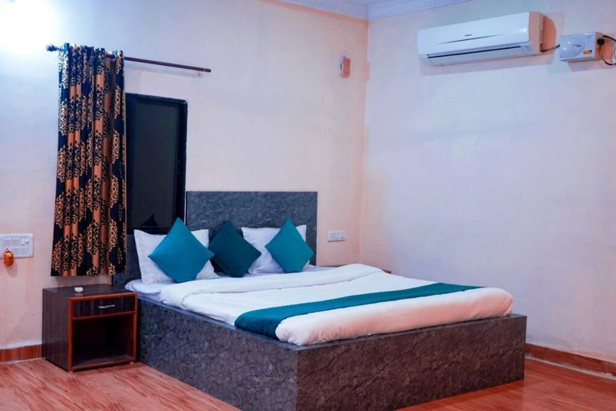 Un dormitorio con cama, mesita de noche, ventana con cortinas, unidad de aire acondicionado e interruptor de luz en la pared.