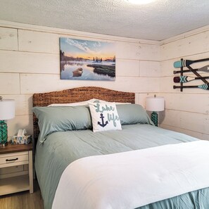 Relax in a serene lakeside-inspired retreat with a large bed, nautical-themed decor, and a wall-mounted paddle rack.