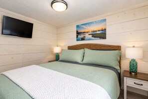 Un dormitorio con una cama, dos mesitas de noche con lámparas, un televisor de pantalla plana en la pared y un cuadro sobre la cama.