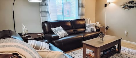Una sala de estar con un sofá de cuero negro, una mesa de centro de madera y un tapete a rayas.