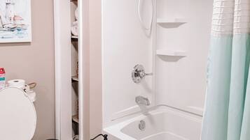 A bathroom with a white bathtub, toilet, and a shelf with toiletries.