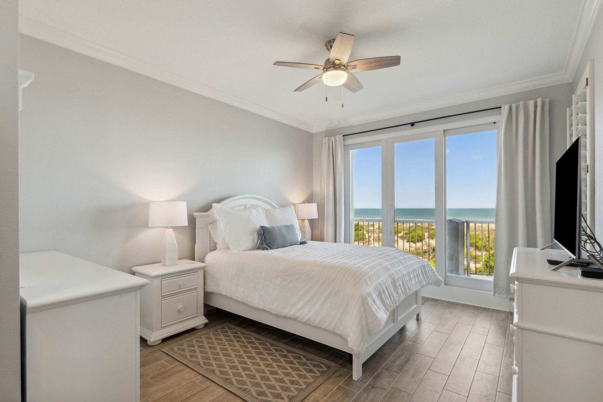 Une chambre à coucher avec un lit, des tables de chevet, un ventilateur de plafond, une télévision et une vue sur la plage.