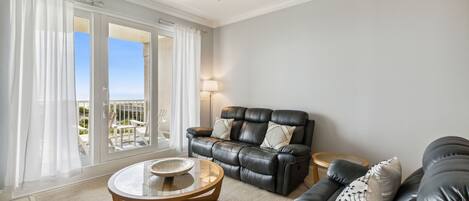 A living room with a black leather sofa, a round coffee table, and a ceiling fan.