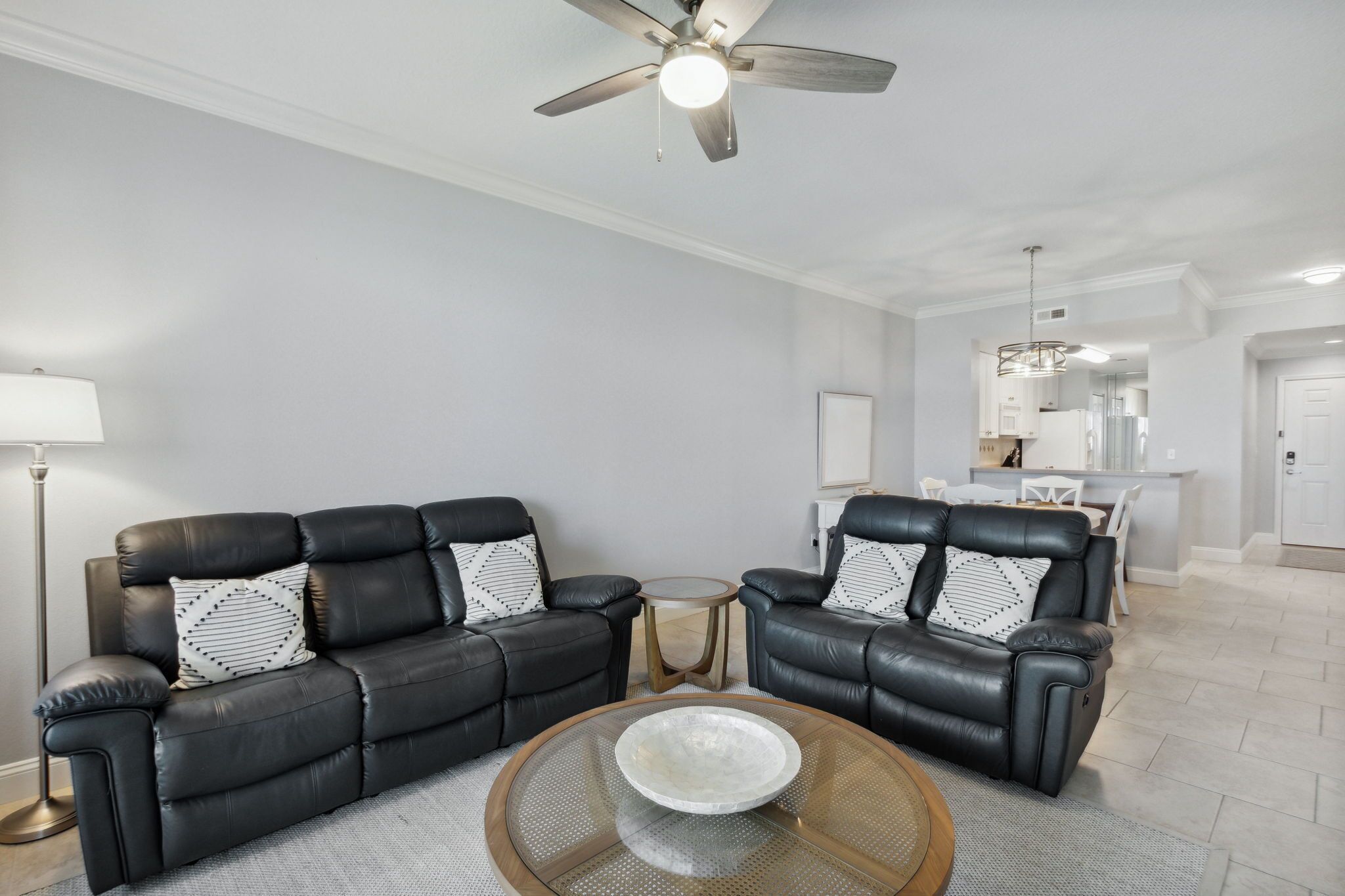 A modern living room with a black leather sofa, a round coffee table, and a ceiling fan.