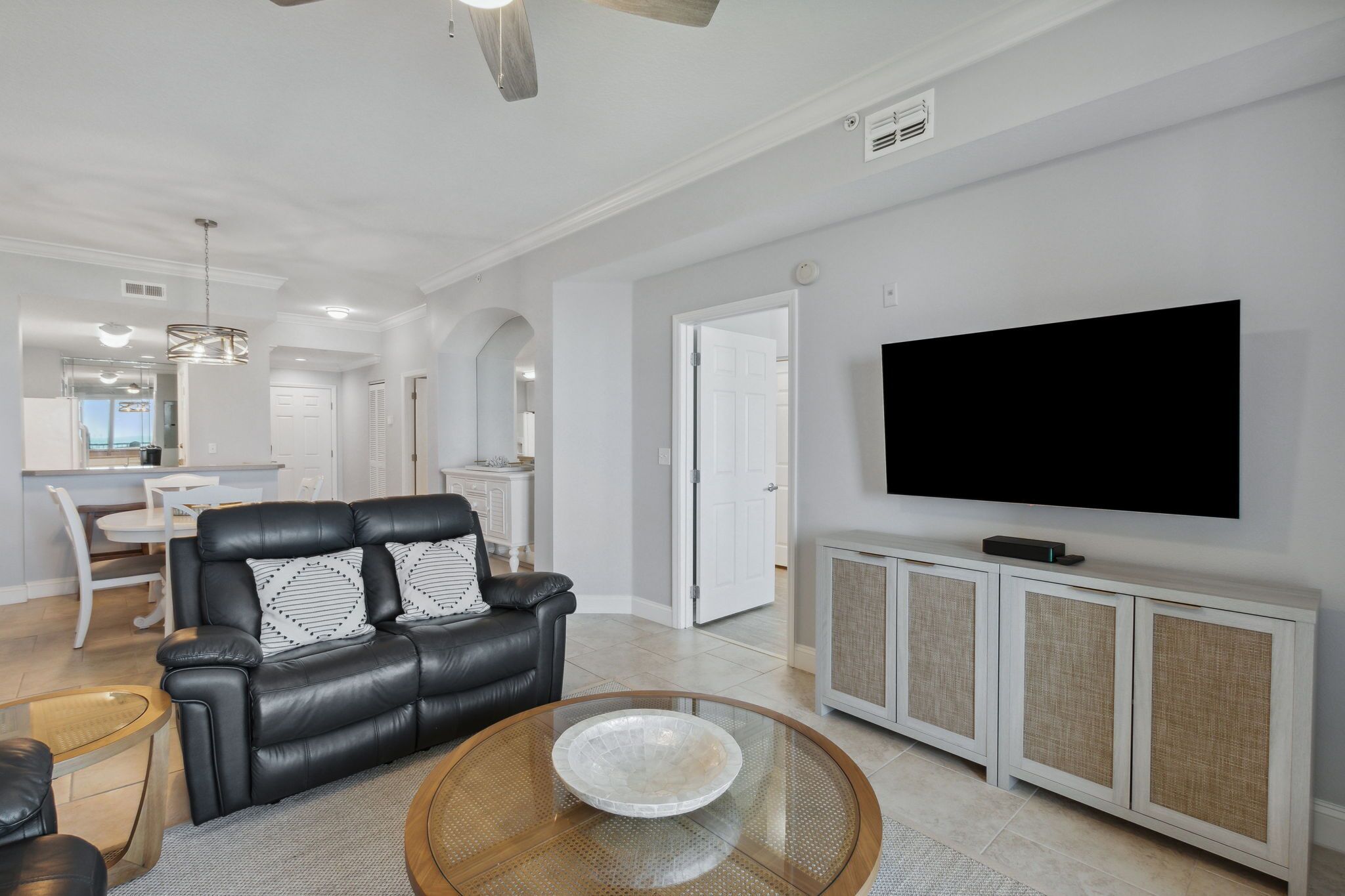 A modern living room with a black leather sofa, a glass coffee table, and a flat-screen TV on a white cabinet.
