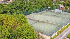 A tennis court surrounded by residential buildings, trees, and mountains in the background. - Borgo del Torchio G23 by Wonderful Italy (Manerba del Garda)