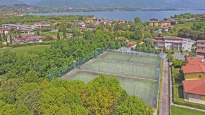 A residential area with multiple buildings, a tennis court, and a lake in the background. - Borgo del Torchio G23 by Wonderful Italy (Manerba del Garda)