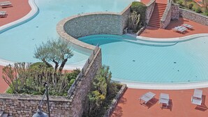 A large, curved swimming pool with a stone wall surrounding it, surrounded by lounge chairs and a stone pathway. - Borgo del Torchio G23 by Wonderful Italy (Manerba del Garda)