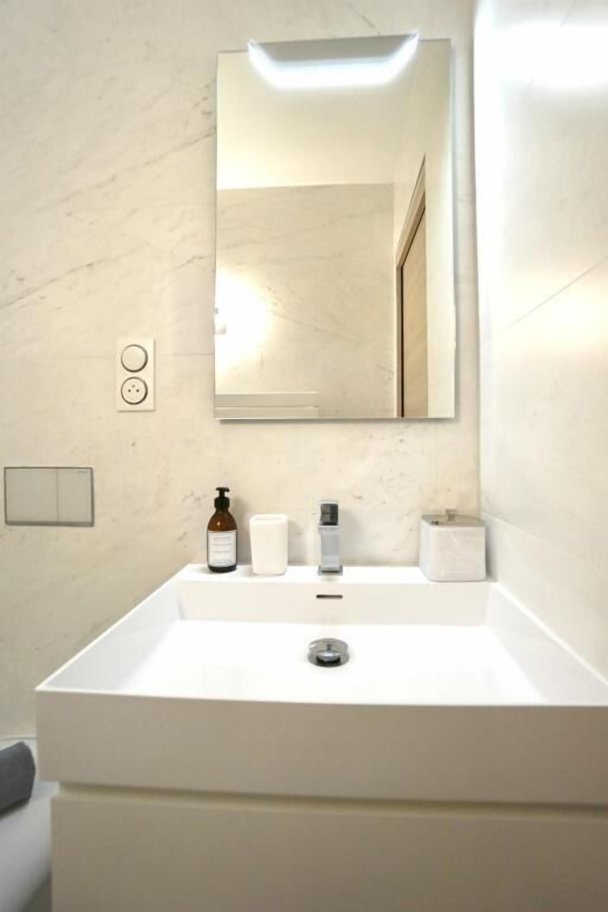 Un baño con un lavabo blanco, un espejo, una botella de jabón, un cepillo de dientes y una toalla.