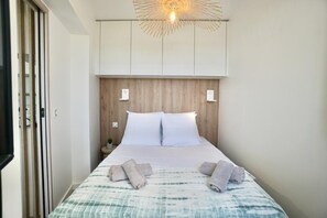 A hotel room with a bed, white headboard, bedside lamps, and a wall-mounted light fixture.